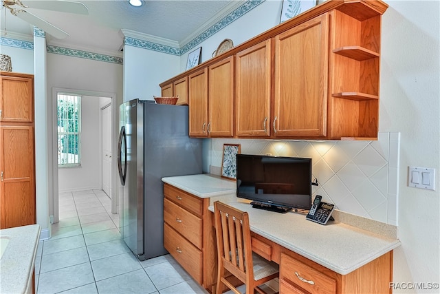 kitchen featuring ceiling fan, stainless steel fridge, decorative backsplash, built in desk, and ornamental molding