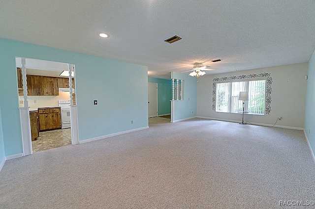 spare room with a textured ceiling, light colored carpet, and ceiling fan