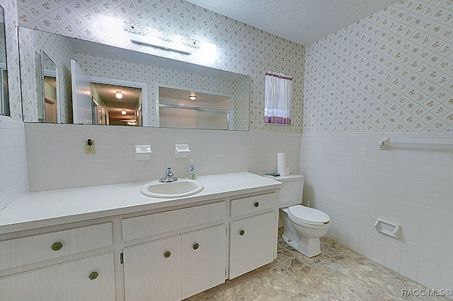 bathroom with walk in shower, a textured ceiling, toilet, vanity, and tile walls