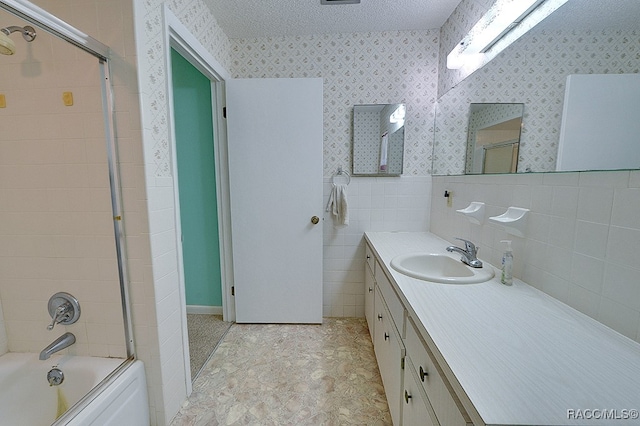 bathroom with tile walls, vanity, bath / shower combo with glass door, and a textured ceiling