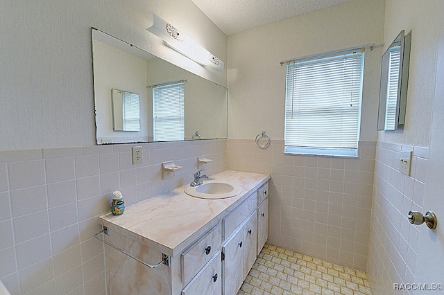 bathroom with a textured ceiling, vanity, and tile walls