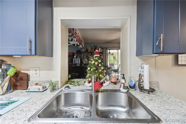 kitchen with light stone countertops, blue cabinets, and sink