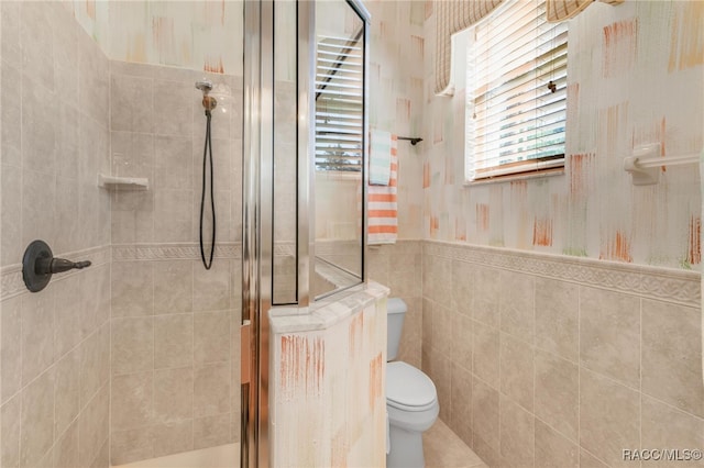 bathroom featuring tiled shower, toilet, and tile walls