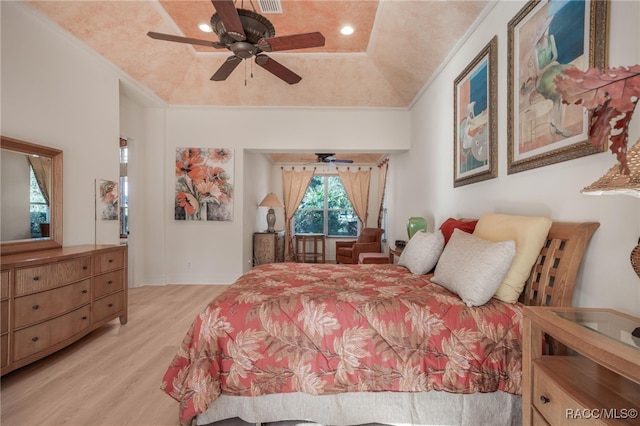 bedroom featuring light hardwood / wood-style floors, ceiling fan, ornamental molding, and a tray ceiling