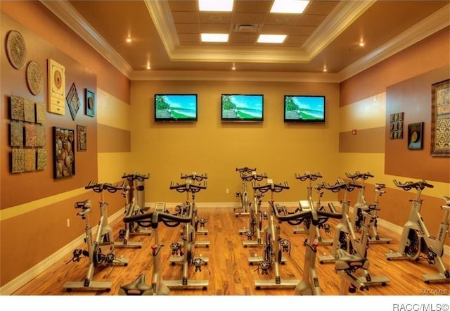 exercise room featuring a tray ceiling, wood-type flooring, and ornamental molding