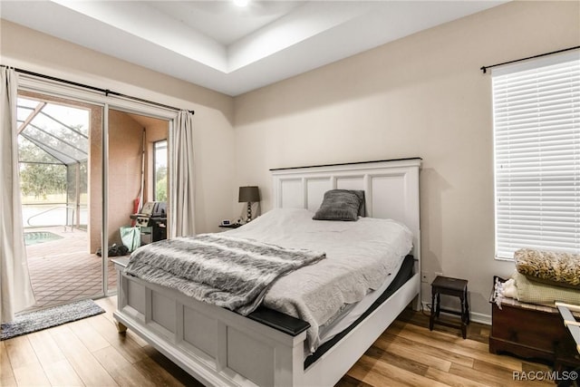 bedroom featuring access to outside, light hardwood / wood-style floors, and a tray ceiling