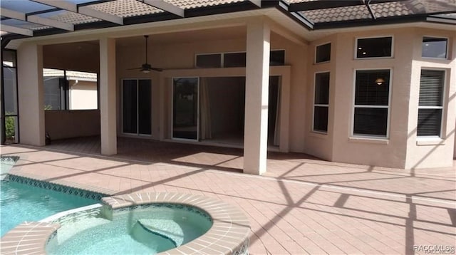 exterior space featuring glass enclosure, an in ground hot tub, ceiling fan, and a patio