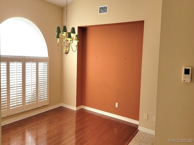 empty room with hardwood / wood-style flooring and a notable chandelier