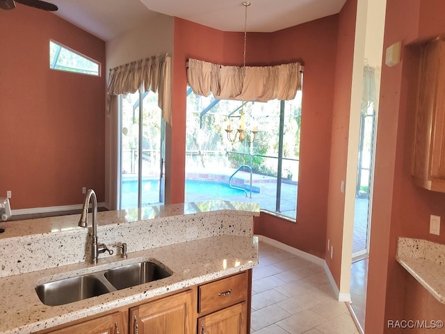 kitchen with light stone counters, sink, light tile patterned floors, and pendant lighting