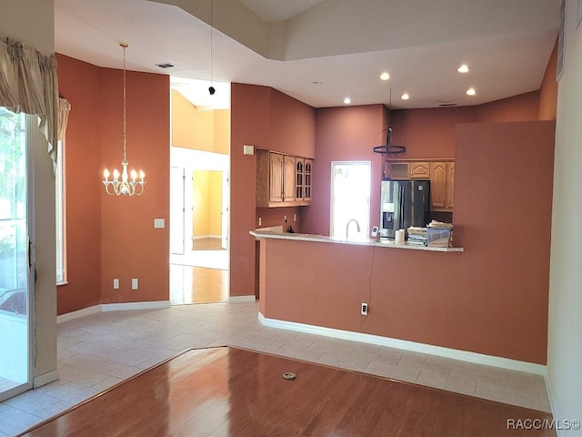 kitchen featuring high vaulted ceiling, hanging light fixtures, light wood-type flooring, refrigerator with ice dispenser, and kitchen peninsula