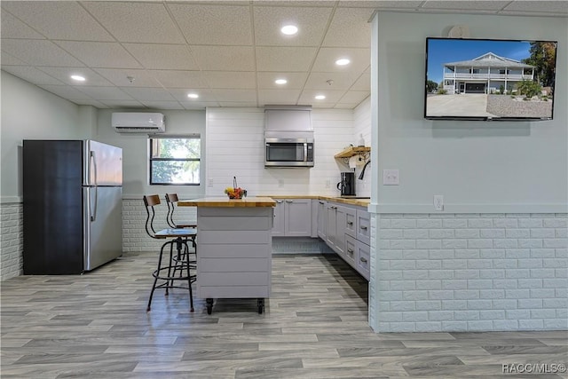 kitchen featuring wooden counters, a wall mounted AC, light wood-style floors, and stainless steel appliances