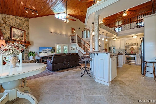 kitchen with wooden ceiling, open floor plan, appliances with stainless steel finishes, decorative columns, and a kitchen breakfast bar