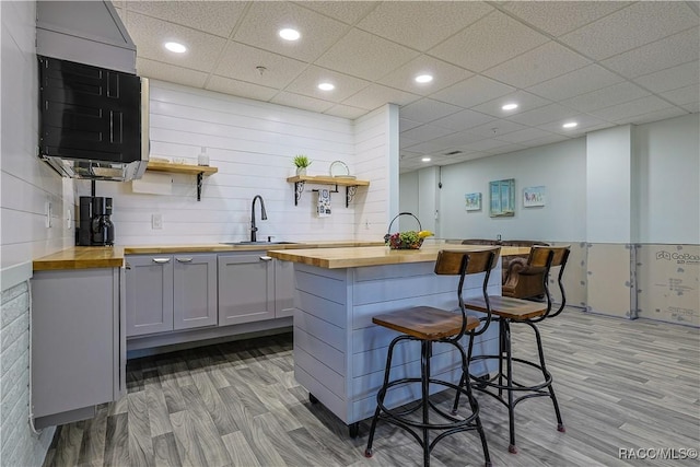 kitchen featuring gray cabinetry, butcher block countertops, a kitchen bar, and open shelves