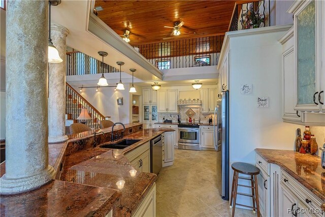 kitchen featuring ceiling fan, ornate columns, wooden ceiling, appliances with stainless steel finishes, and a sink