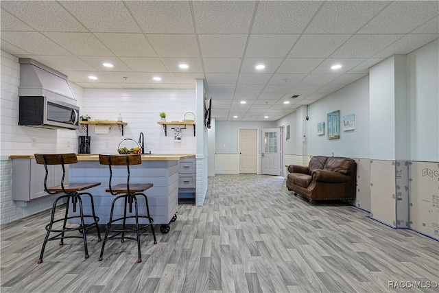 kitchen featuring light wood-style floors, a kitchen bar, butcher block counters, open shelves, and stainless steel microwave