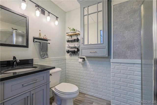 bathroom with toilet, vanity, wood finished floors, a wainscoted wall, and a shower with shower door