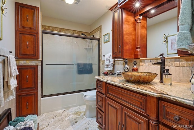 bathroom featuring toilet, enclosed tub / shower combo, vanity, and backsplash