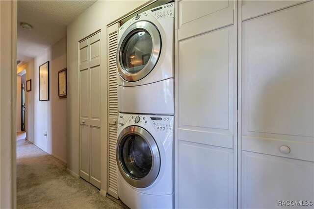 laundry area with baseboards, a textured ceiling, stacked washer / dryer, laundry area, and light colored carpet