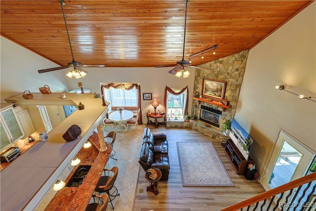 living area with a stone fireplace, wood ceiling, a ceiling fan, and wood finished floors