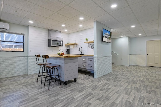 kitchen featuring stainless steel microwave, butcher block countertops, light wood-type flooring, open shelves, and a kitchen bar