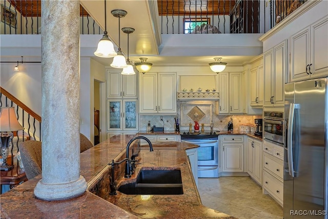 kitchen featuring a towering ceiling, dark stone countertops, a sink, stainless steel appliances, and decorative backsplash