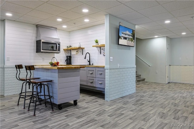 kitchen featuring a sink, light wood-style floors, stainless steel microwave, butcher block countertops, and a breakfast bar area