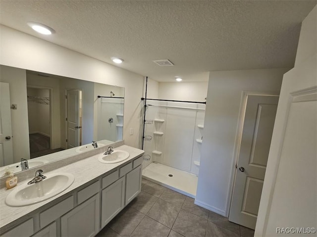 bathroom featuring a textured ceiling, walk in shower, vanity, and tile patterned flooring