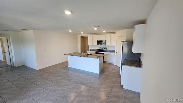 kitchen with an island with sink, stainless steel appliances, dark stone counters, white cabinets, and sink