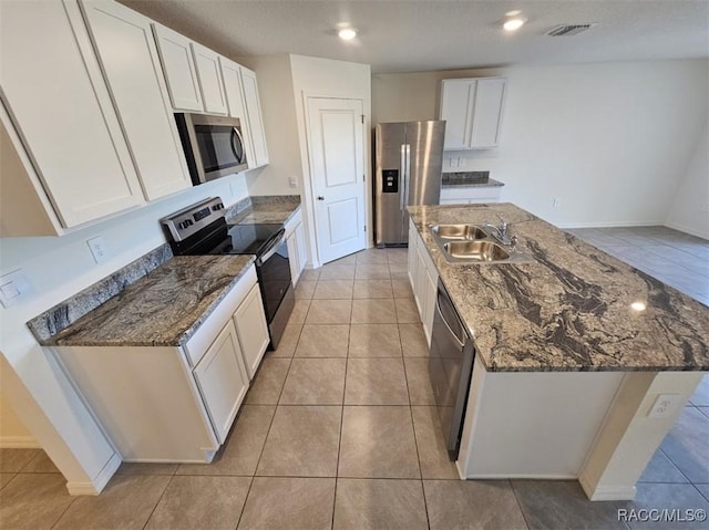 kitchen with white cabinets, stainless steel appliances, an island with sink, sink, and light tile patterned floors