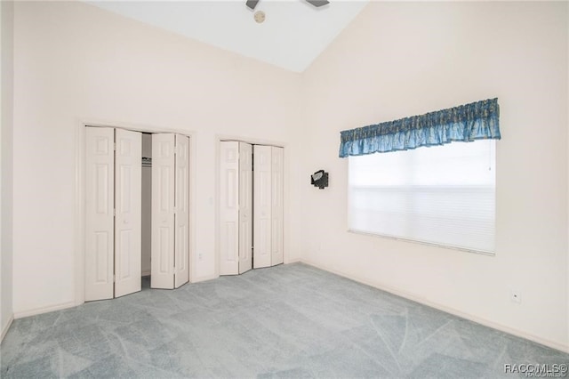 unfurnished bedroom with multiple closets, high vaulted ceiling, and light colored carpet