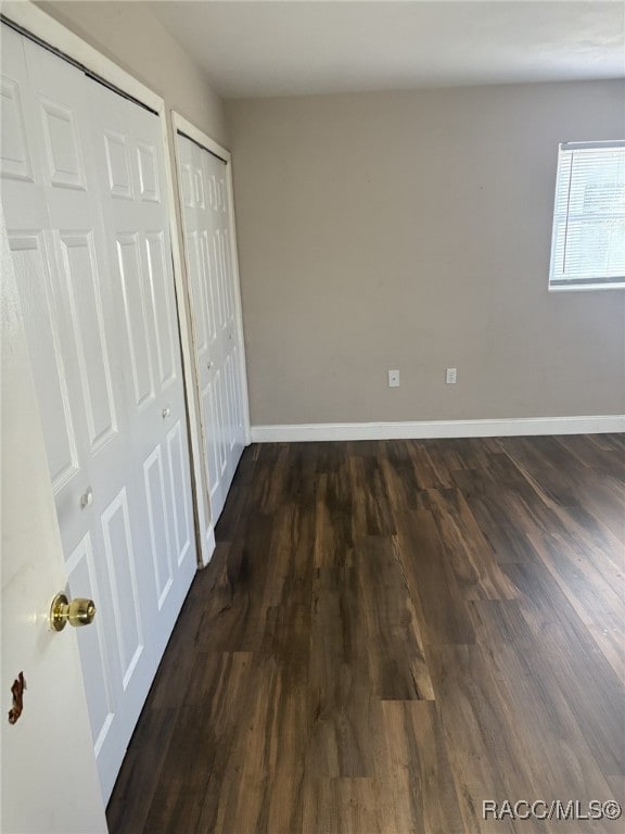 unfurnished bedroom featuring dark wood-type flooring and two closets