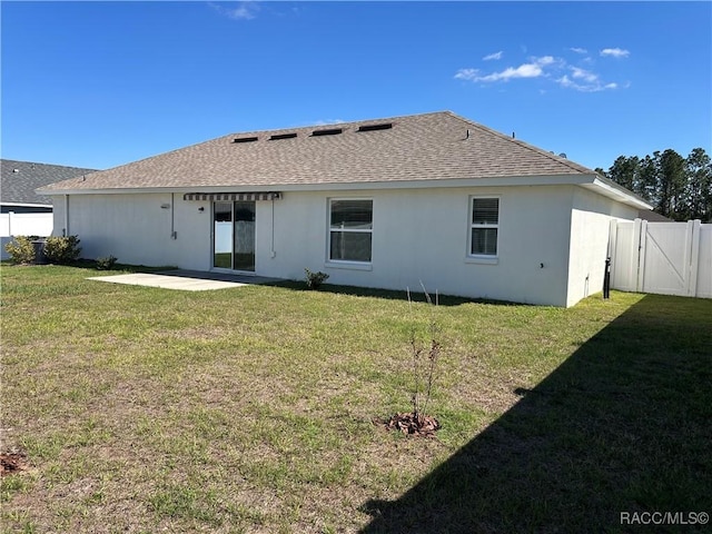 rear view of property featuring fence, roof with shingles, a lawn, a gate, and a patio area