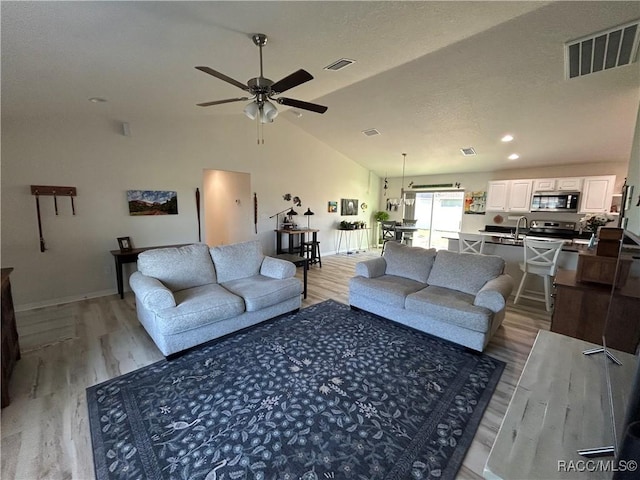 living area with high vaulted ceiling, light wood-type flooring, visible vents, and a ceiling fan