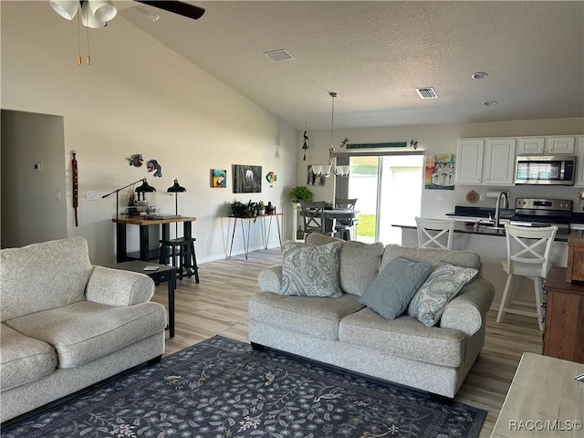 living room with high vaulted ceiling, visible vents, a textured ceiling, and light wood finished floors