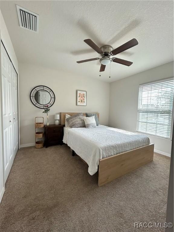 bedroom with a textured ceiling, dark colored carpet, a closet, and visible vents