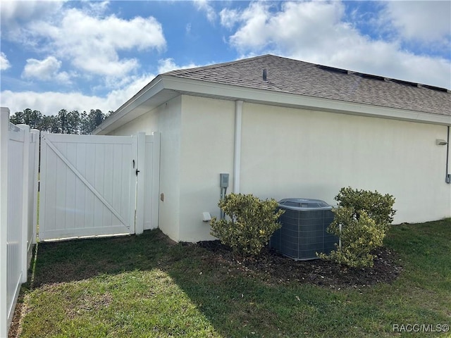 view of side of home featuring a yard, a gate, central AC unit, and roof with shingles