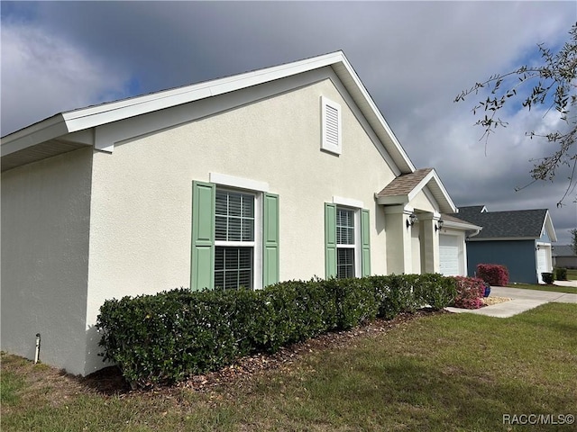 view of side of home with a garage, a lawn, and stucco siding