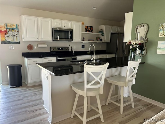 kitchen with stainless steel appliances, dark countertops, white cabinets, a sink, and a kitchen bar