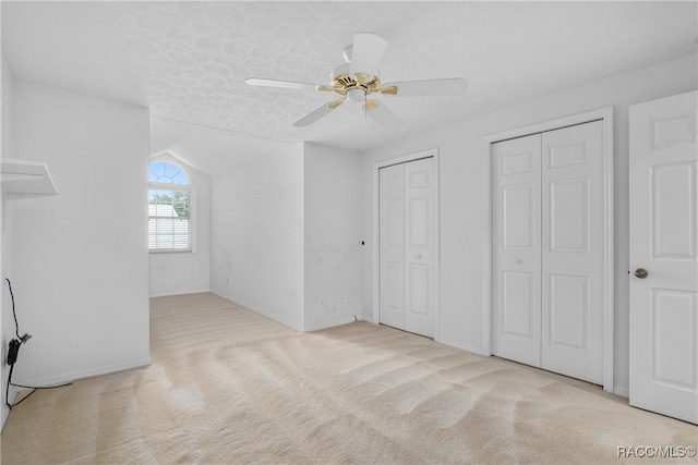 unfurnished bedroom with ceiling fan, light colored carpet, a textured ceiling, vaulted ceiling, and two closets