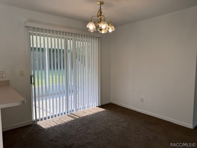 spare room featuring dark carpet and a chandelier