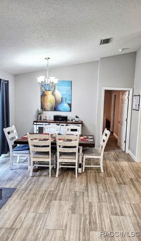 dining space with a textured ceiling, wood-type flooring, lofted ceiling, and a notable chandelier