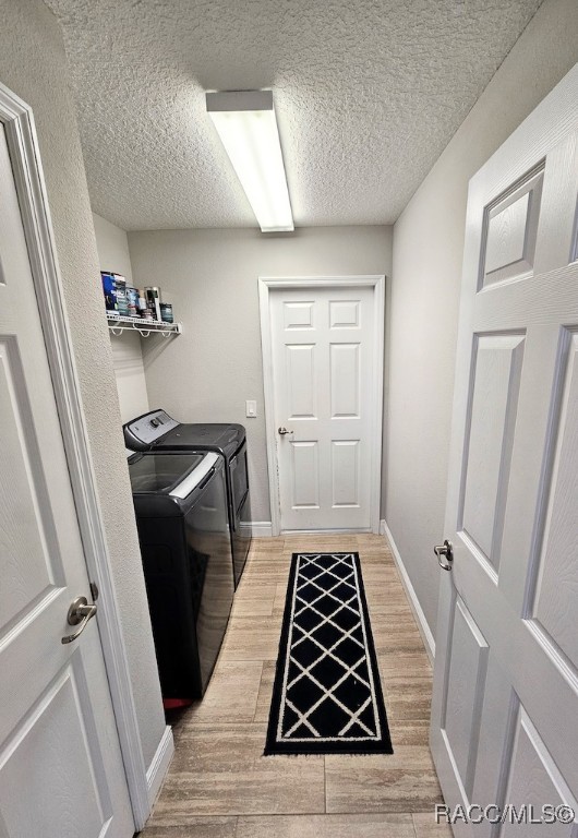 clothes washing area with light hardwood / wood-style floors, a textured ceiling, and washing machine and clothes dryer