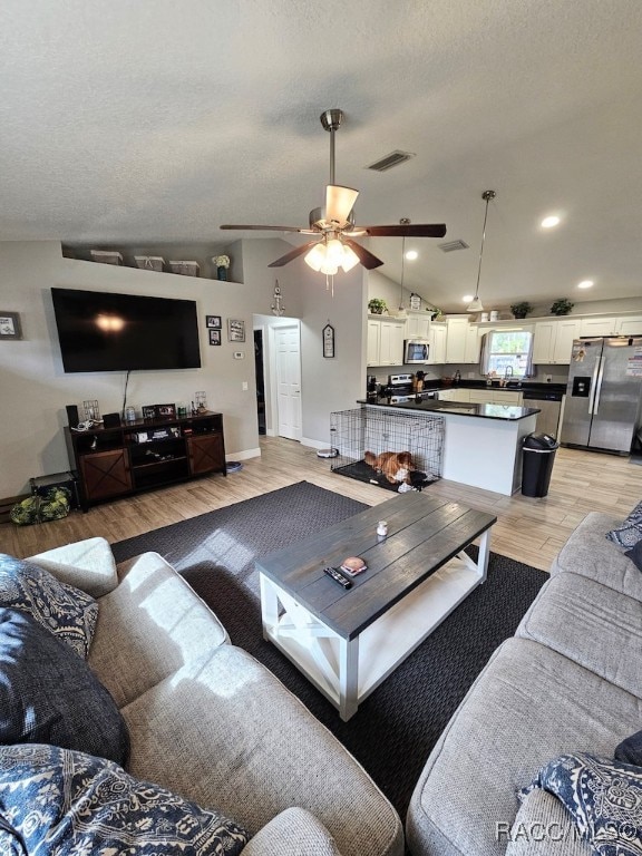 living room featuring ceiling fan, light wood-type flooring, a textured ceiling, and vaulted ceiling