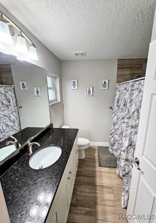 bathroom with hardwood / wood-style floors, vanity, toilet, and a textured ceiling