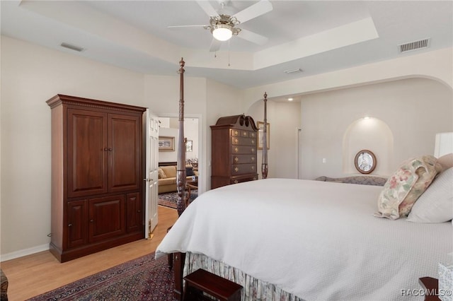 bedroom with light wood-style flooring, a raised ceiling, a ceiling fan, and visible vents