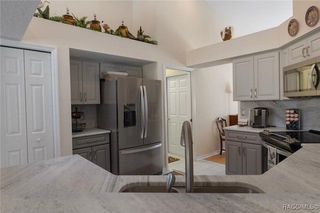 kitchen with a sink, appliances with stainless steel finishes, gray cabinetry, and light stone countertops