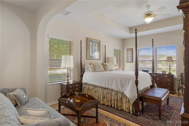 bedroom featuring ceiling fan, multiple windows, baseboards, and wood finished floors