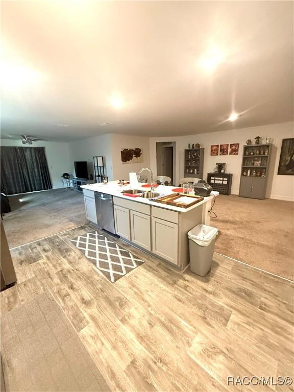 kitchen featuring gray cabinets, an island with sink, sink, stainless steel dishwasher, and light hardwood / wood-style floors