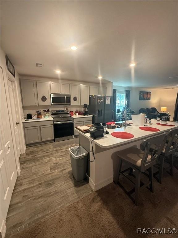 kitchen with gray cabinets, hardwood / wood-style floors, an island with sink, a kitchen bar, and stainless steel appliances