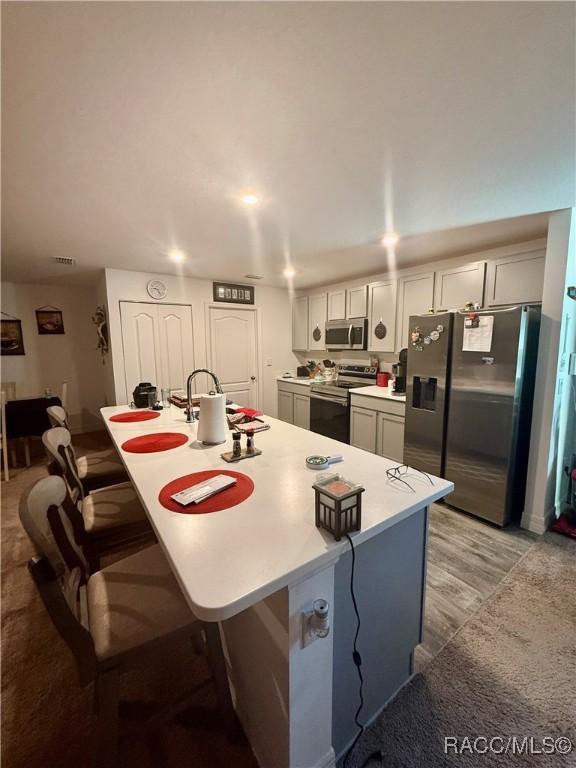 kitchen with appliances with stainless steel finishes, a breakfast bar, a kitchen island with sink, and light wood-type flooring